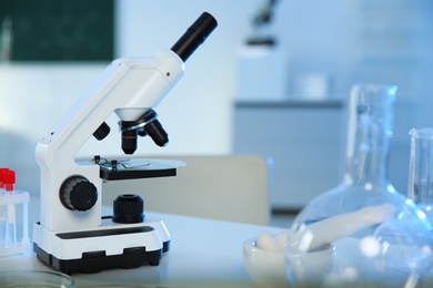 Photo of Professional microscope and glassware on table in chemistry laboratory, space for text