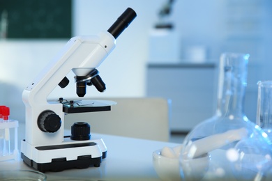 Professional microscope and glassware on table in chemistry laboratory, space for text