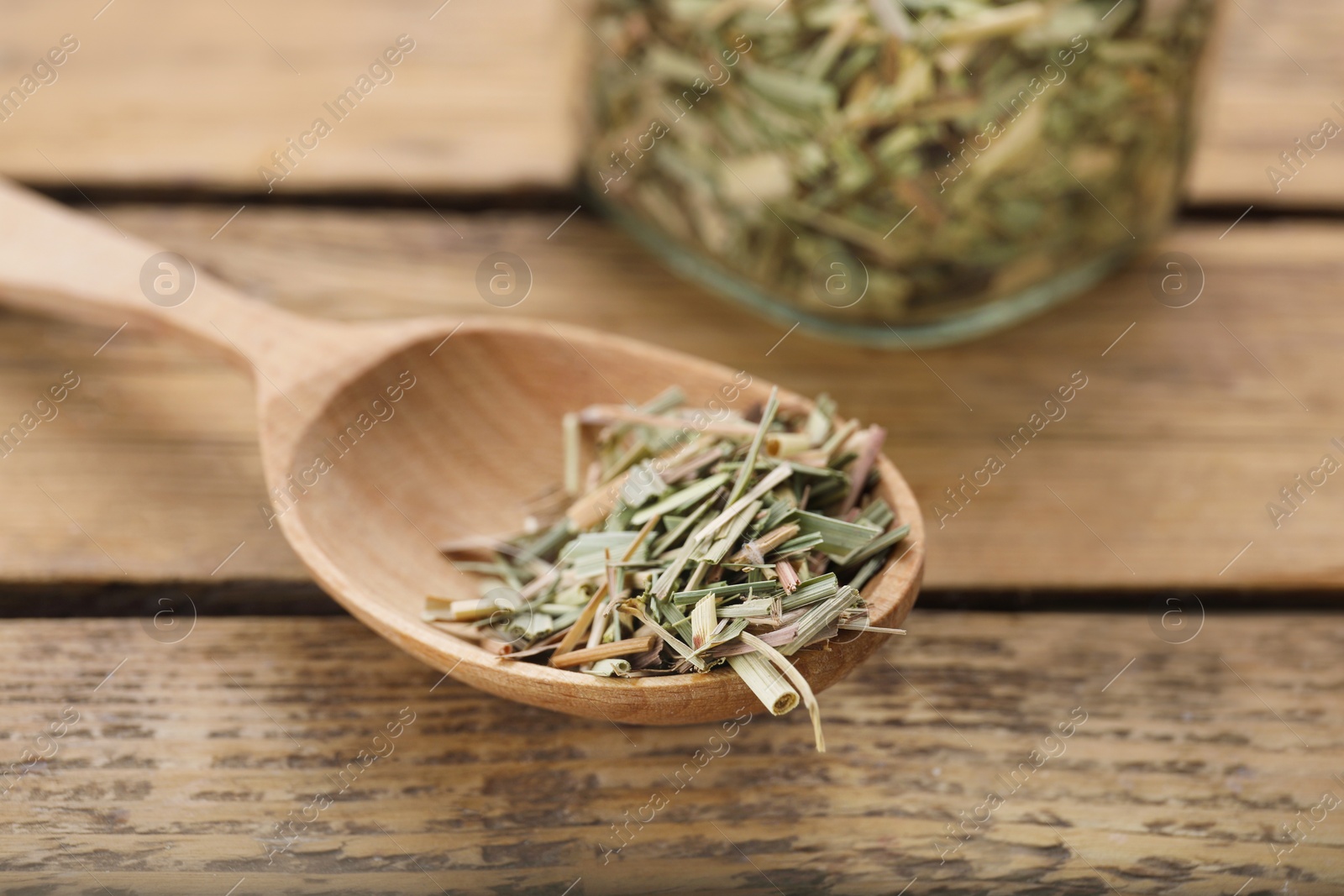 Photo of Spoon with aromatic dried lemongrass on wooden table, closeup