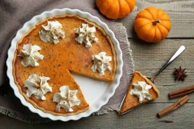 Delicious pumpkin pie with whipped cream and spices on wooden table, flat lay
