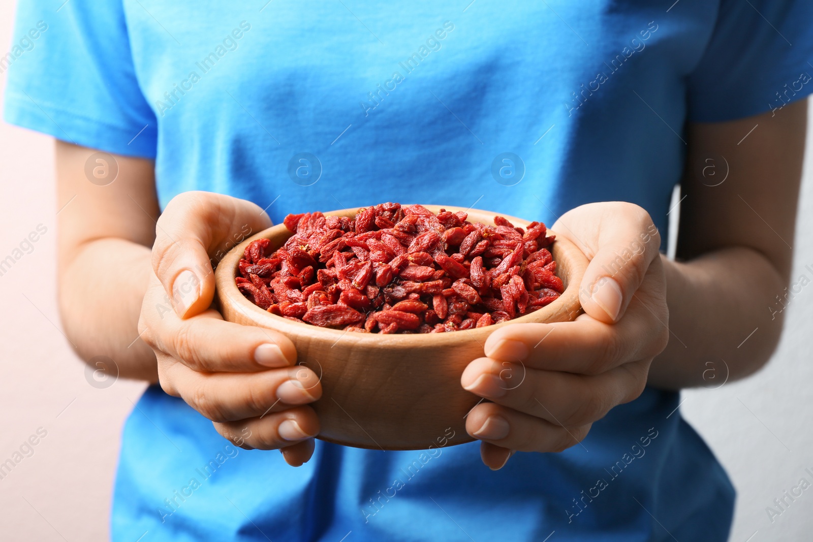 Photo of Woman holding bowl of red dried goji berries, closeup