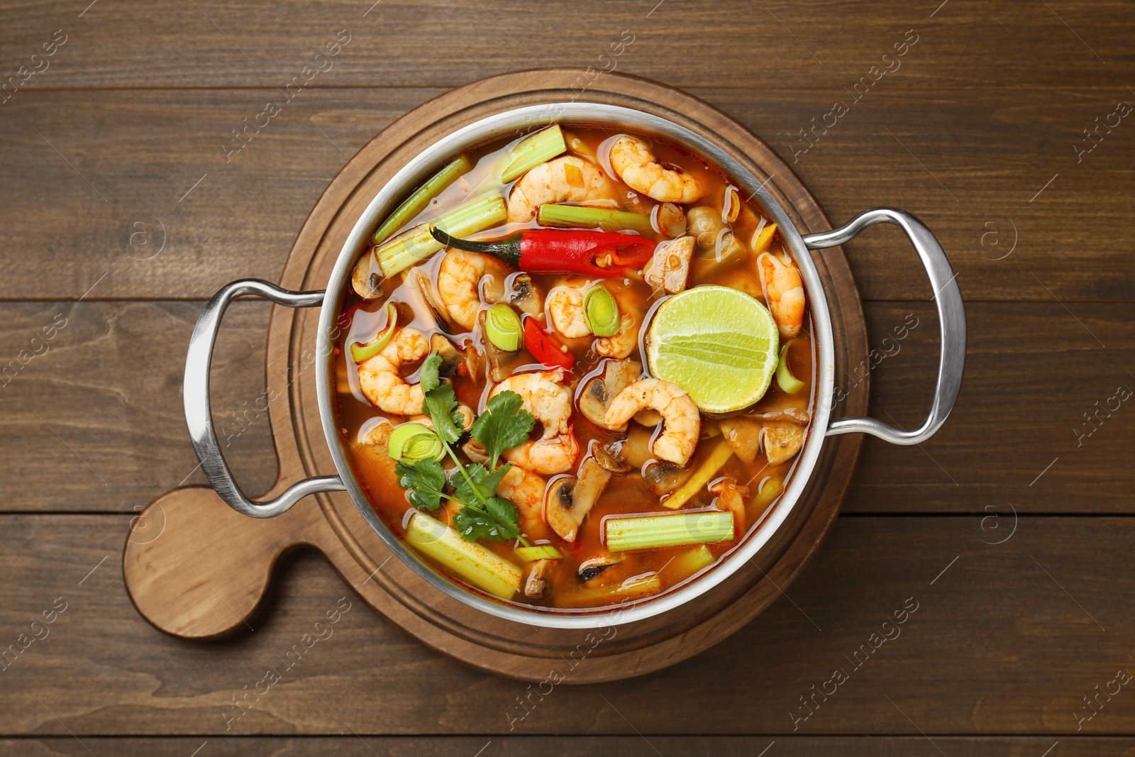 Photo of Saucepan with delicious Tom Yum soup on wooden table, top view