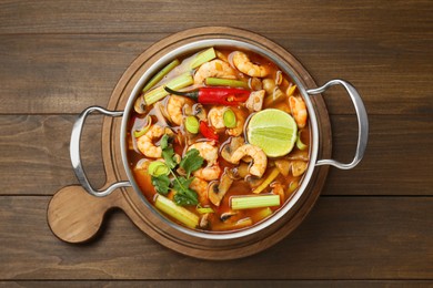 Photo of Saucepan with delicious Tom Yum soup on wooden table, top view