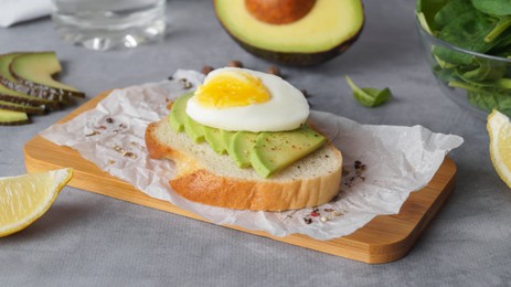 Photo of Delicious sandwich with boiled egg, pieces of avocado and lemon wedge on gray table