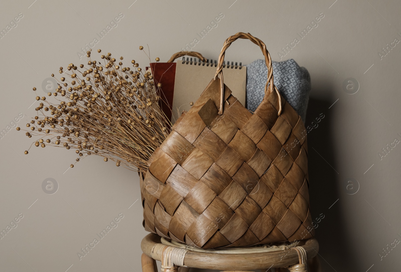 Photo of Stylish straw bag with beautiful dried flowers on chair near grey wall