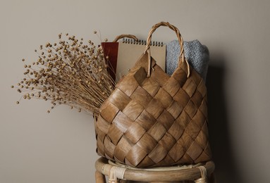 Photo of Stylish straw bag with beautiful dried flowers on chair near grey wall