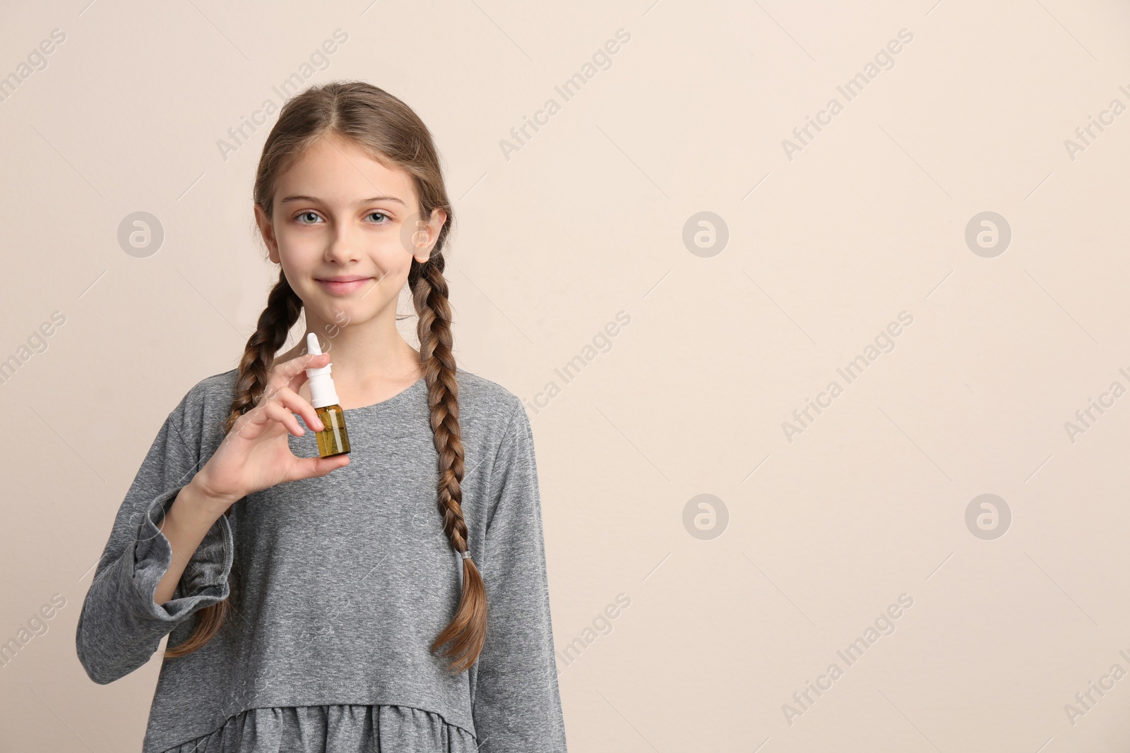 Photo of Sick little girl with nasal spray on beige background. Space for text