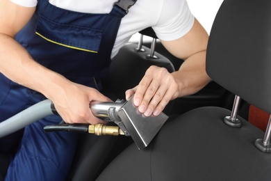 Male worker removing dirt from car seat with professional vacuum cleaner