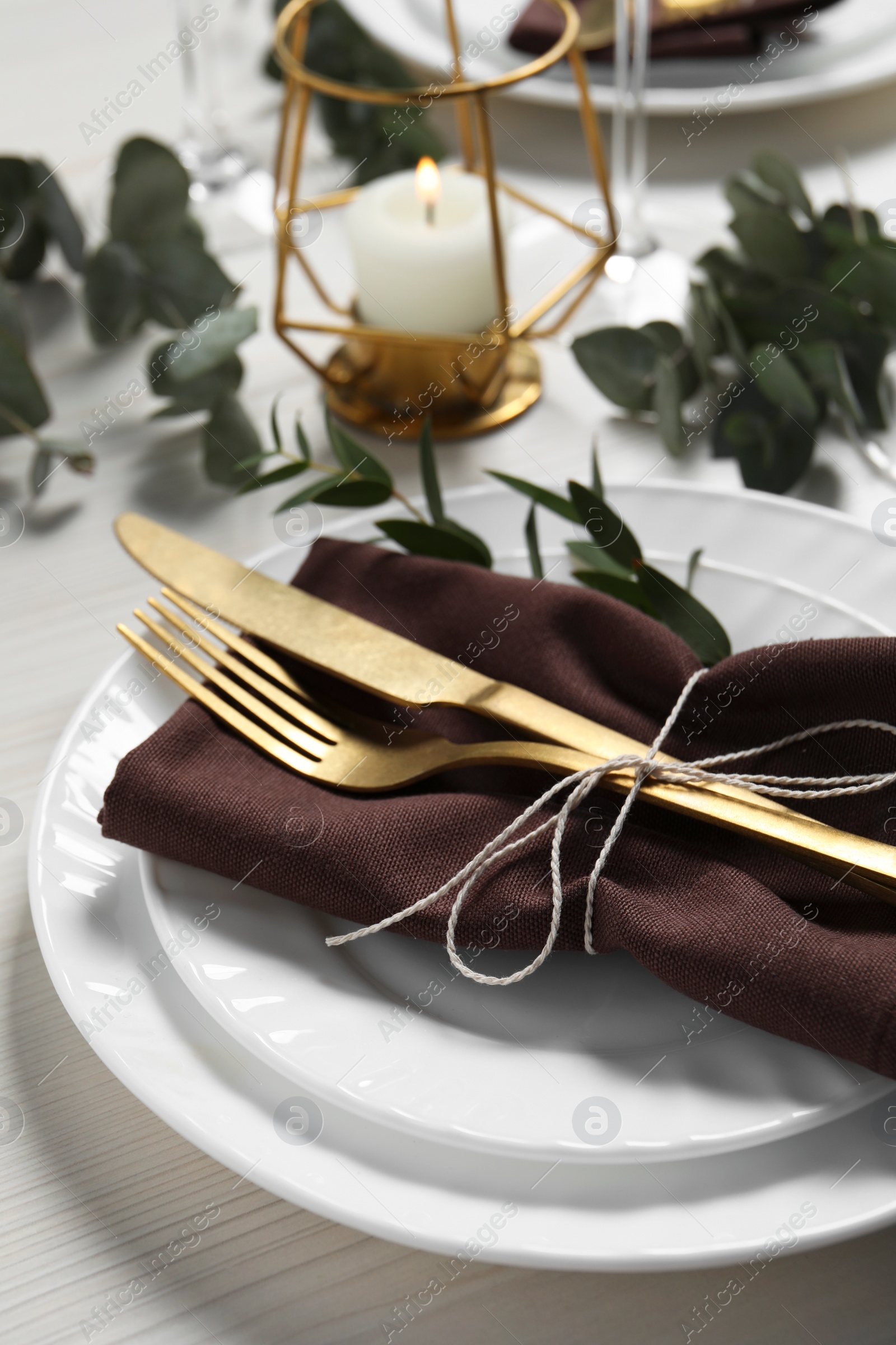 Photo of Stylish setting with cutlery and eucalyptus leaves on white wooden table, closeup