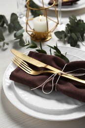 Photo of Stylish setting with cutlery and eucalyptus leaves on white wooden table, closeup