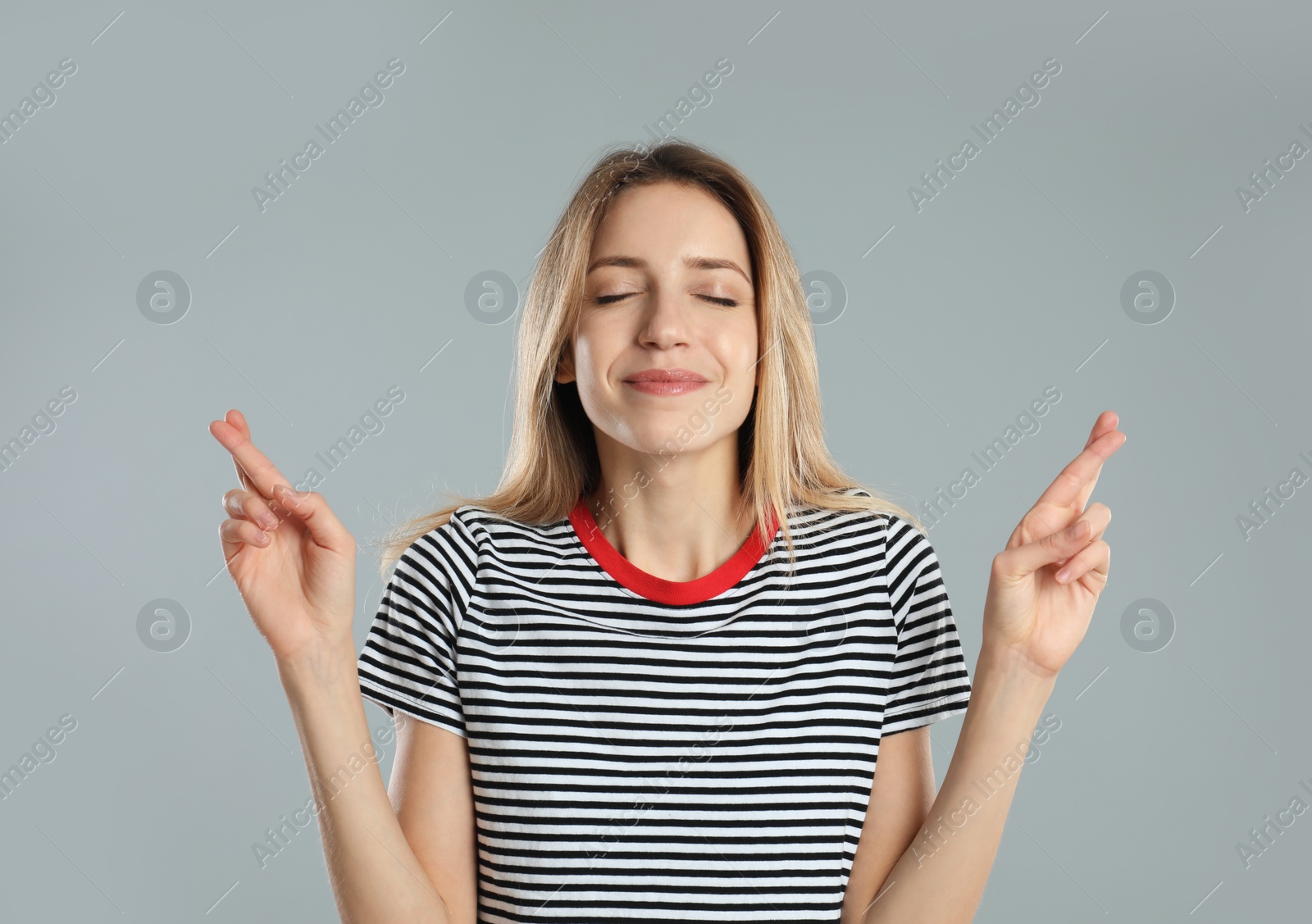 Photo of Woman with crossed fingers on light grey background. Superstition concept