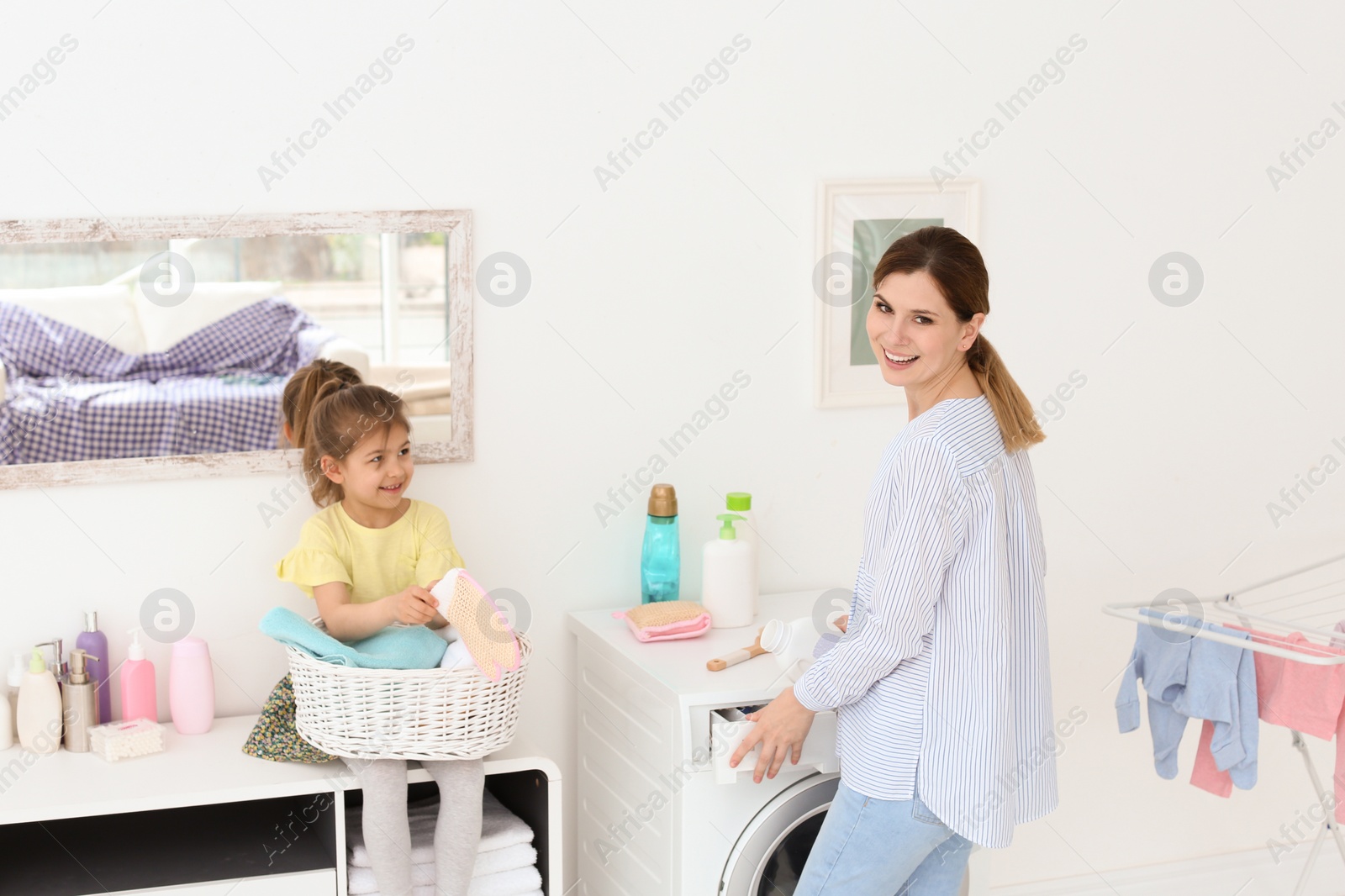 Photo of Housewife with little daughter doing laundry at home