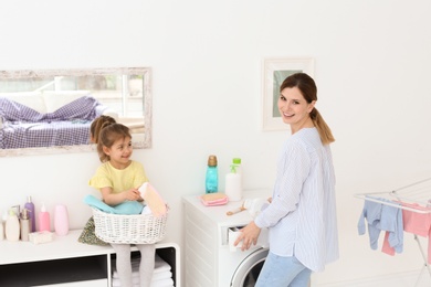 Housewife with little daughter doing laundry at home