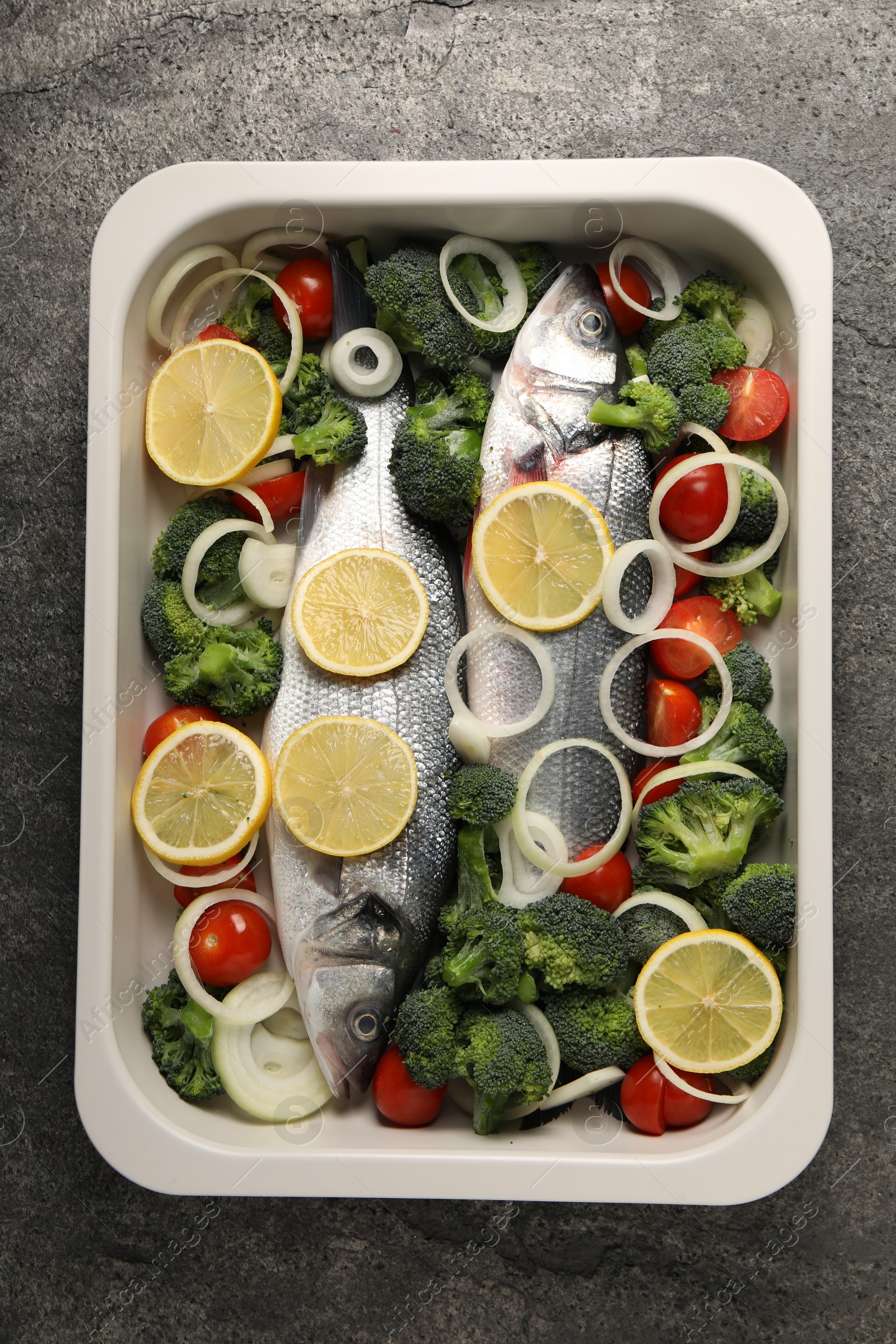 Photo of Raw fish with vegetables and lemon in baking dish on grey table, top view