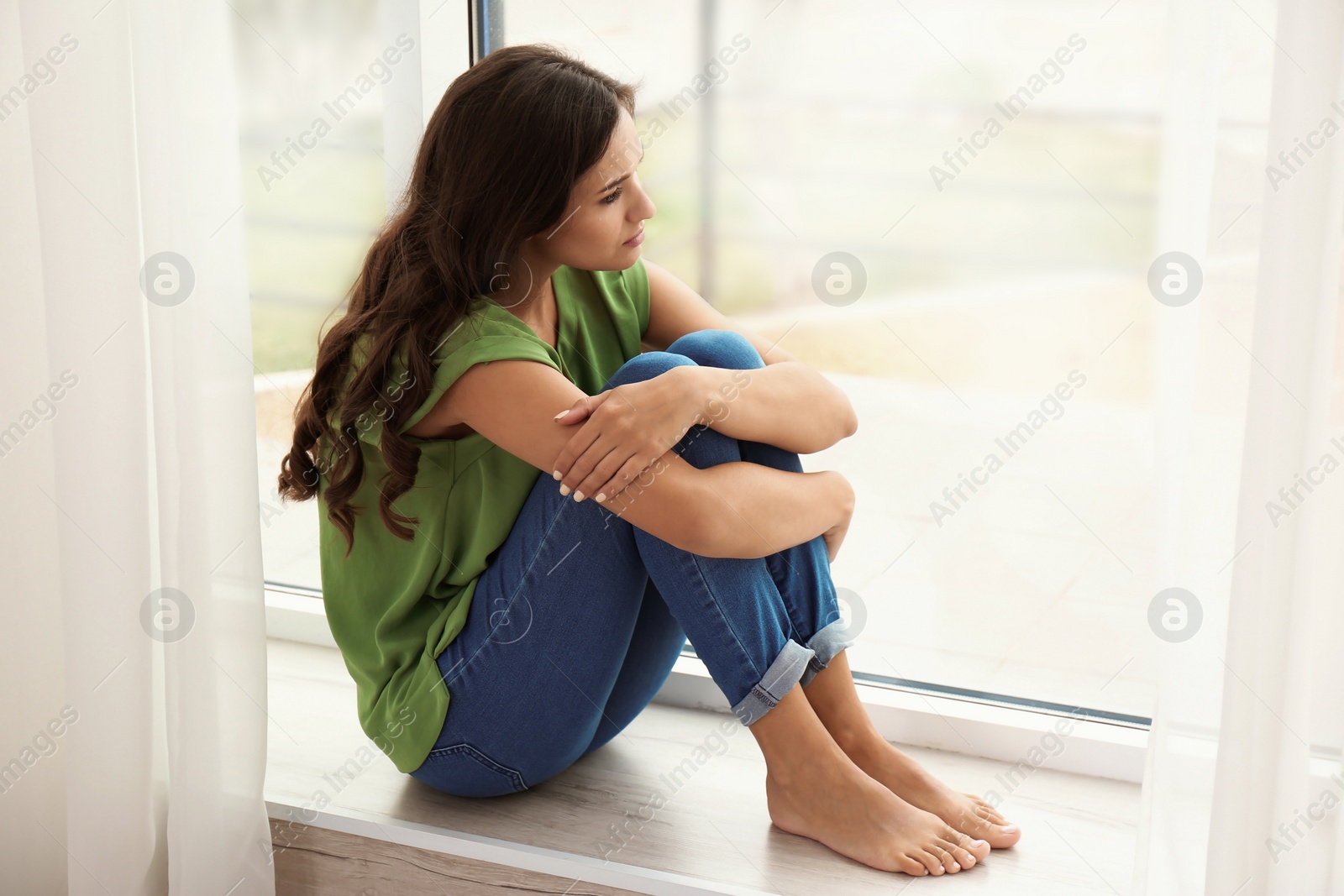 Photo of Young sad woman sitting near window at home