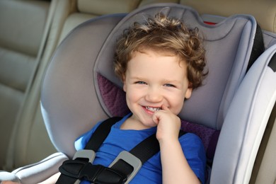Photo of Cute little boy sitting in child safety seat inside car
