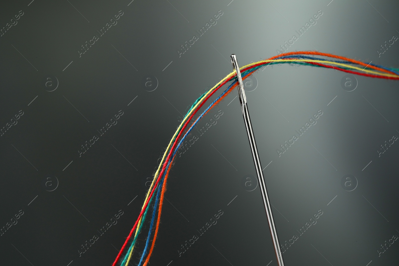Photo of Sewing needle with colorful threads on dark background, space for text