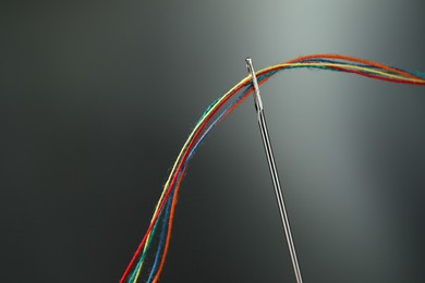 Sewing needle with colorful threads on dark background, space for text