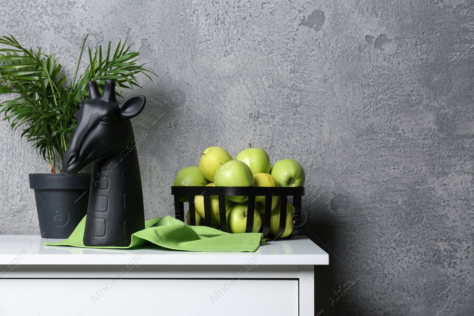 Photo of Stylish decor, basket of apples and houseplant on white table near grey wall indoors, space for text. Interior design