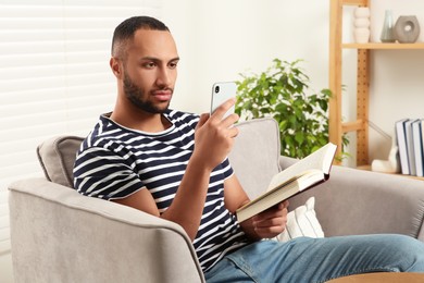 Young man using smartphone while reading book at home. Internet addiction