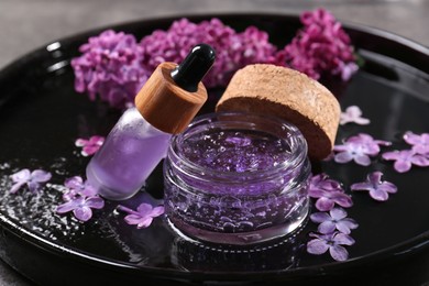 Photo of Cosmetic products and lilac flowers on black tray