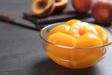 Glass bowl with conserved peach halves on grey table. Space for text