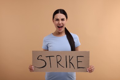 Photo of Angry woman holding cardboard banner with word Strike on beige background