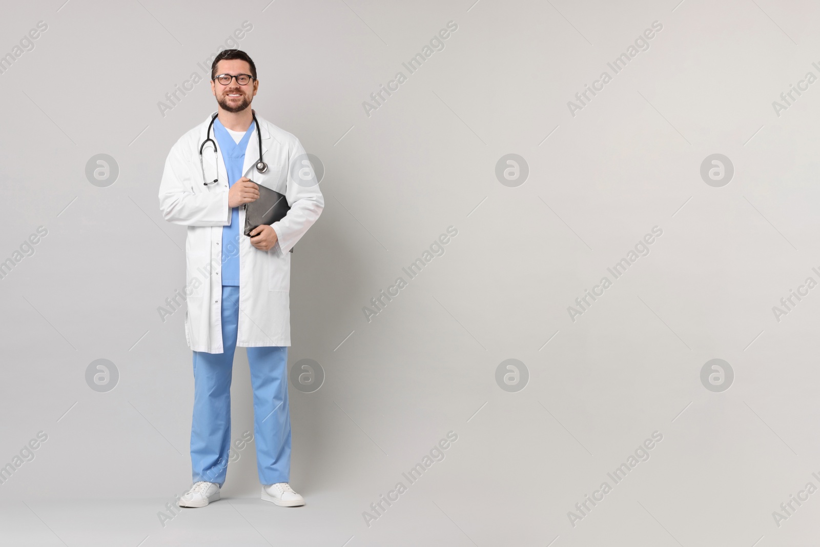 Photo of Smiling doctor with clipboard on light grey background. Space for text