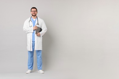 Photo of Smiling doctor with clipboard on light grey background. Space for text