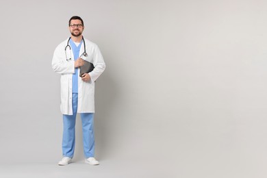 Smiling doctor with clipboard on light grey background. Space for text