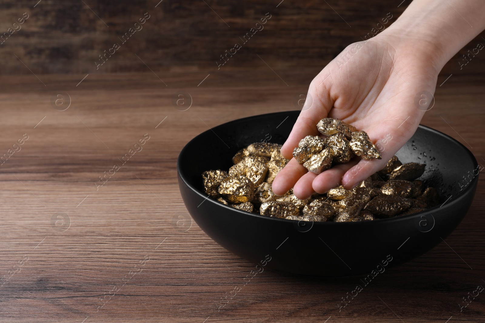 Photo of Woman with gold nuggets at wooden table, closeup. Space for text