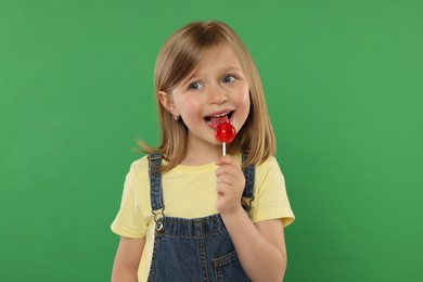 Photo of Portrait of cute girl licking lollipop on green background
