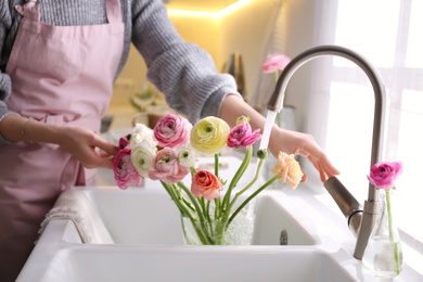 Photo of Woman taking care of cut fresh ranunculus flowers in kitchen, closeup
