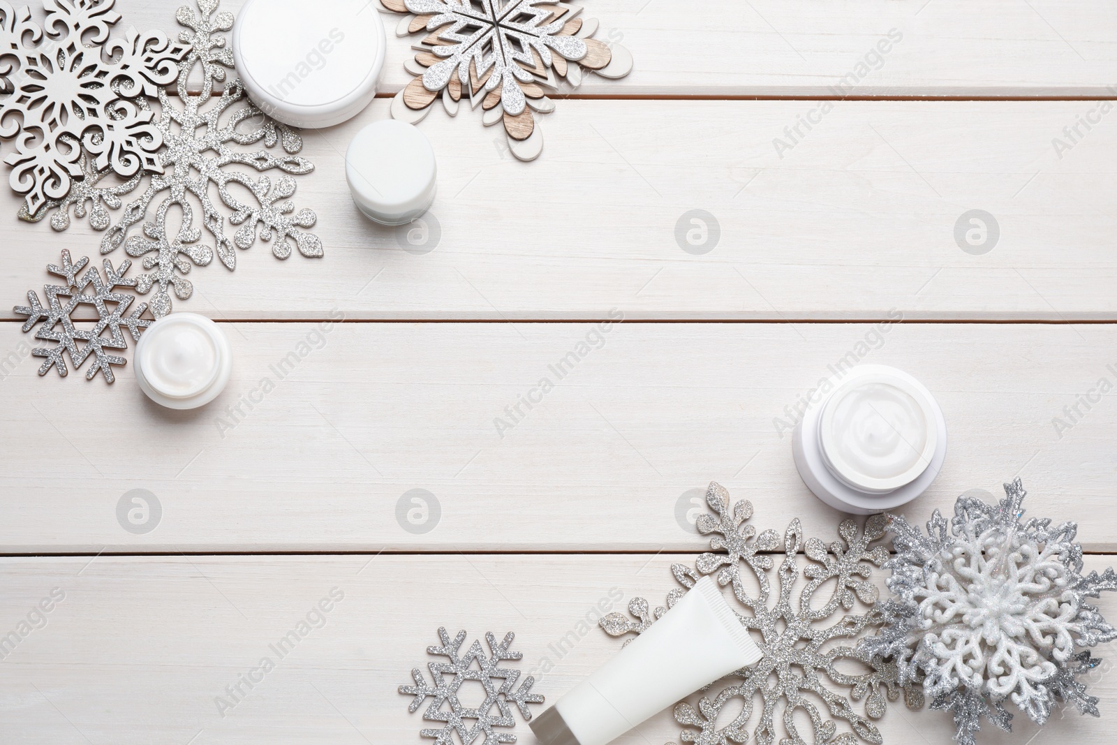 Photo of Flat lay composition with cosmetic products and snowflakes on white wooden table, space for text. Winter skin care