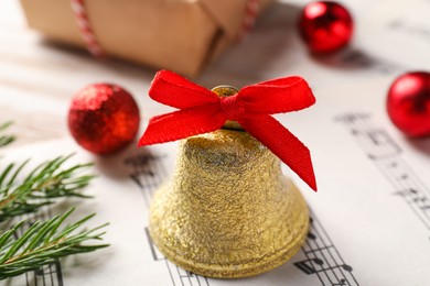 Golden shiny bell with red bow and music sheet on table, closeup. Christmas decoration