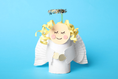 Toy angel made of toilet paper hub on light blue background