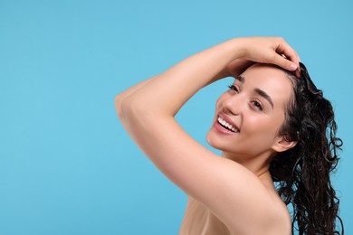 Photo of Beautiful happy woman washing hair on light blue background. Space for text