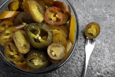 Photo of Glass bowl and fork with slices of pickled green jalapeno peppers on grey table, flat lay