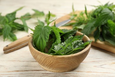 Fresh stinging nettle leaves in bowl on white wooden table