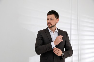 Man wearing stylish suit and cufflinks near white wall, space for text
