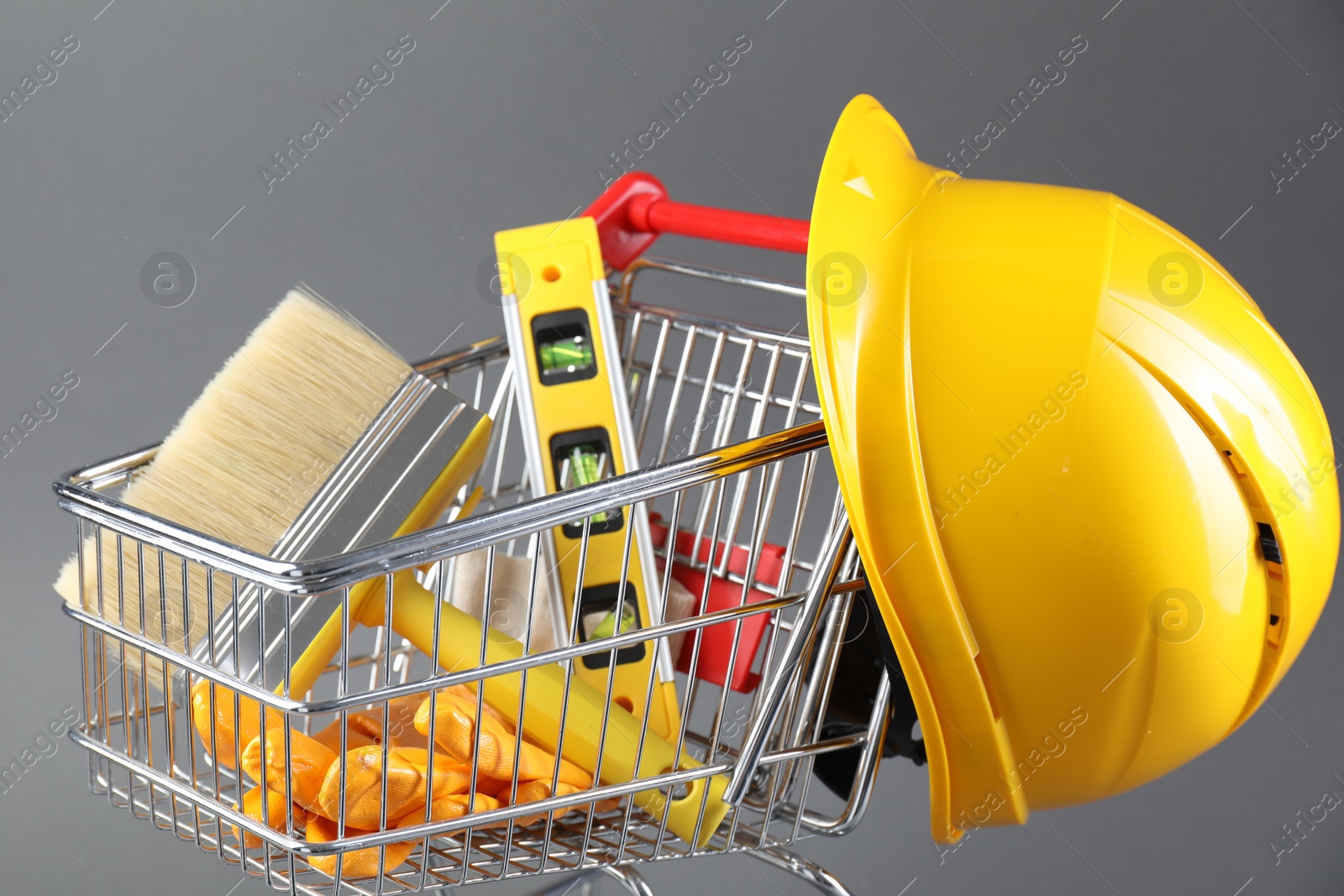 Photo of Small shopping cart with construction level, brush, gloves and hard hat on grey background