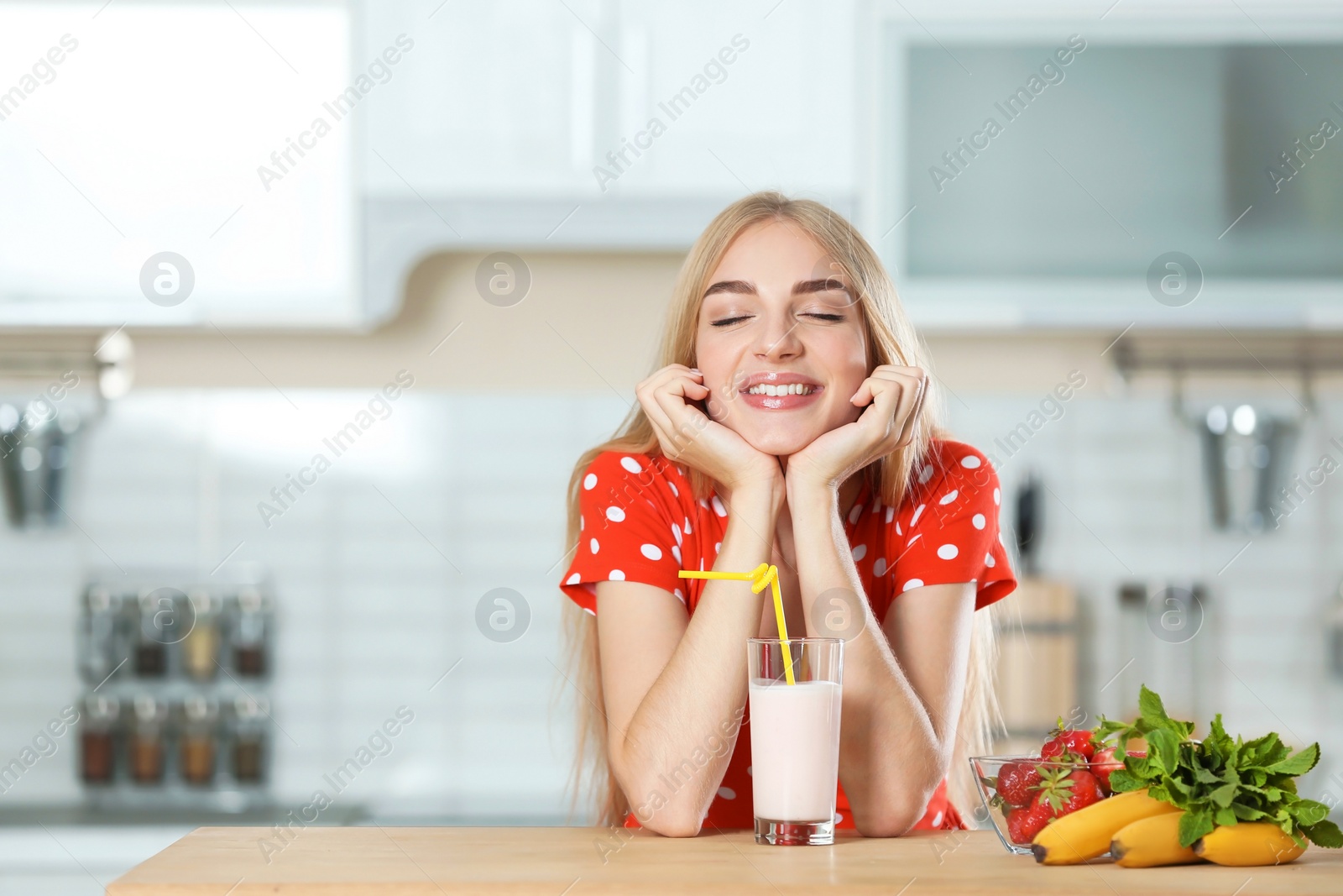 Photo of Young woman with glass of delicious milk shake in kitchen