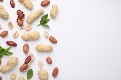 Fresh peanuts and leaves on white table, flat lay. Space for text