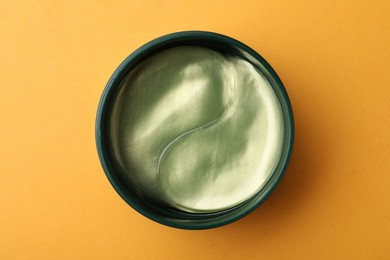 Photo of Under eye patches in jar on orange background, top view. Cosmetic product