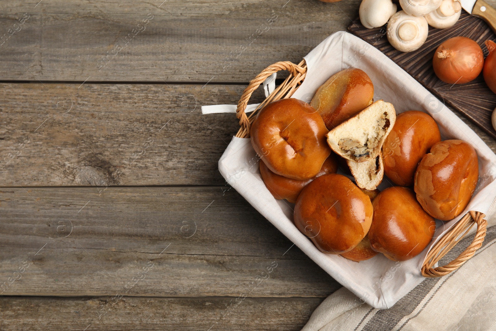 Photo of Wicker basket with delicious baked mushrooms and onion pirozhki on wooden table, flat lay. Space for text