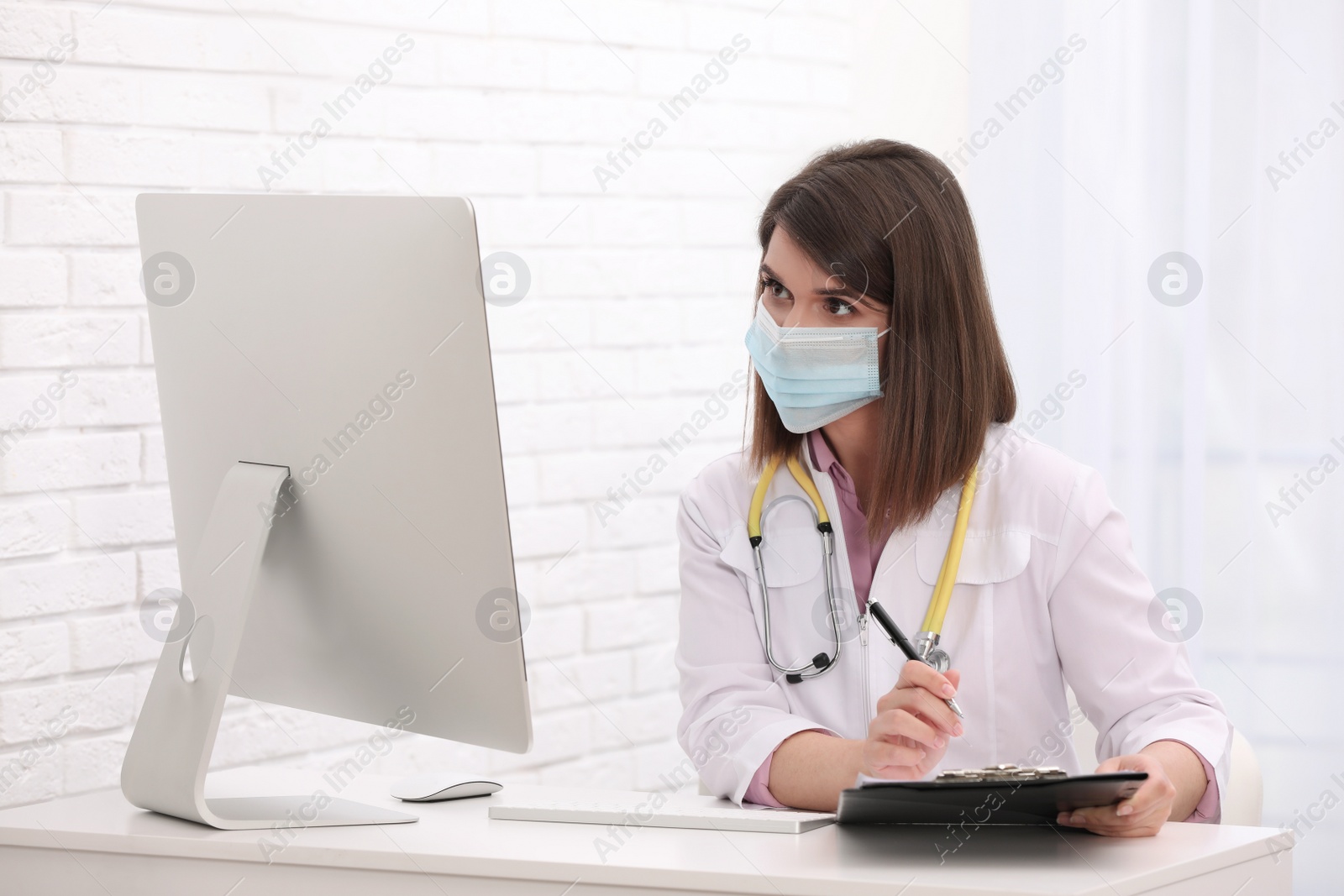 Photo of Pediatrician in protective mask consulting patient online at table indoors