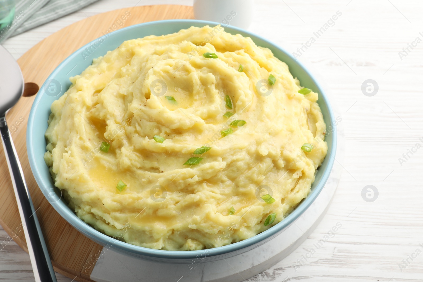 Photo of Bowl of tasty mashed potatoes with onion served on white wooden table, closeup