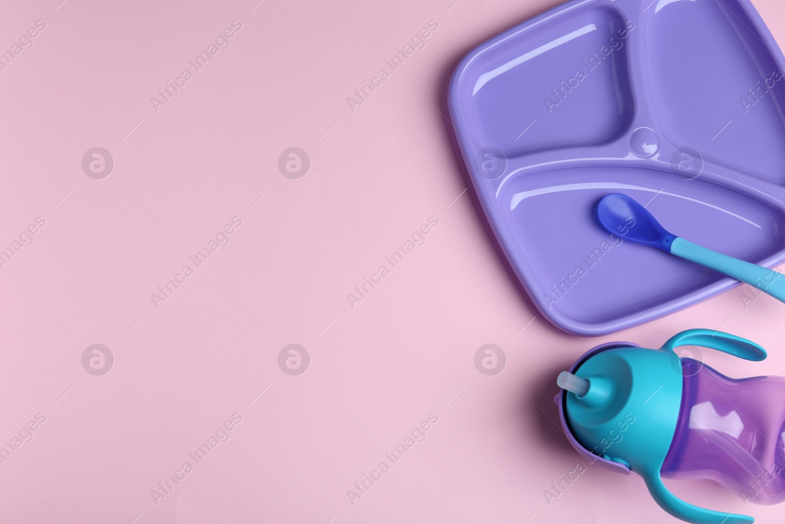 Photo of Set of colorful plastic dishware on light pink background, flat lay with space for text. Serving baby food