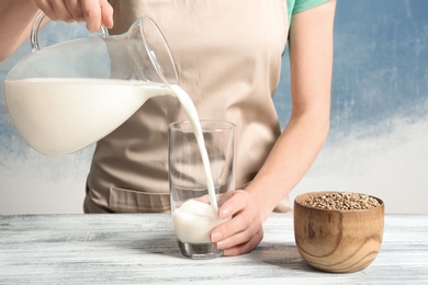 Photo of Woman pouring hemp milk into glass on table, closeup
