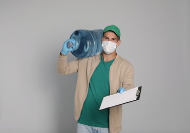 Courier in medical mask with bottle for water cooler and clipboard on light grey background. Delivery during coronavirus quarantine